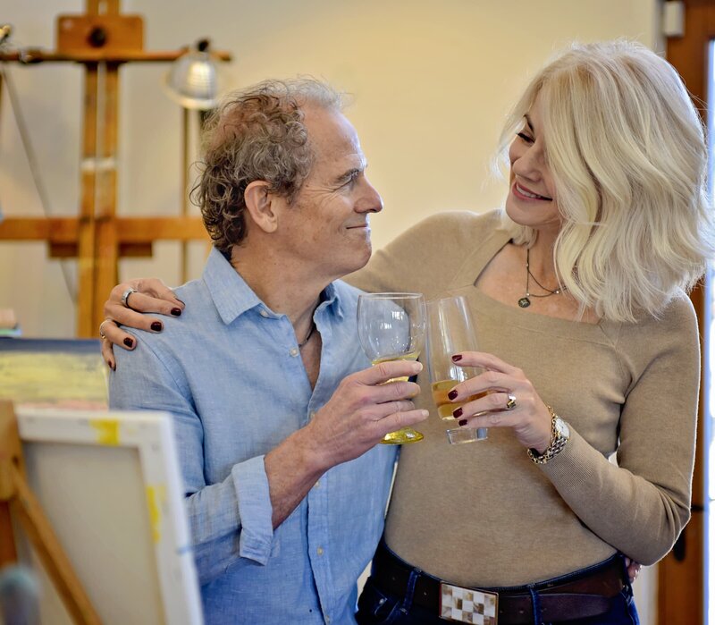 man and woman with their arms around each other clinking wine glasses