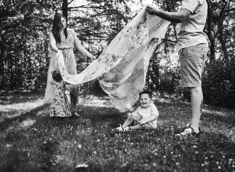 A playful family moment captured in black and white, featuring a child and parents with flowing fabric