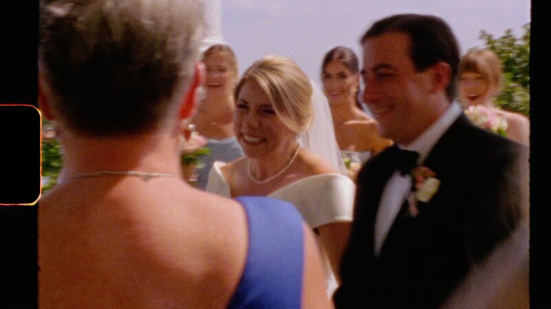 a bride and groom smile happily as they recess down the aisle after getting married and the bridesmaid look on in delight - a still image from Super 8 film
