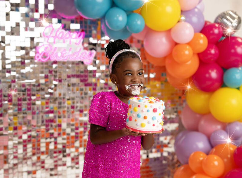 Disco backdrop and vibrant balloons with girl eating cake for her 5th birthday photoshoot. Atlanta kid photo studio decorates birthday sets for all age groups. 