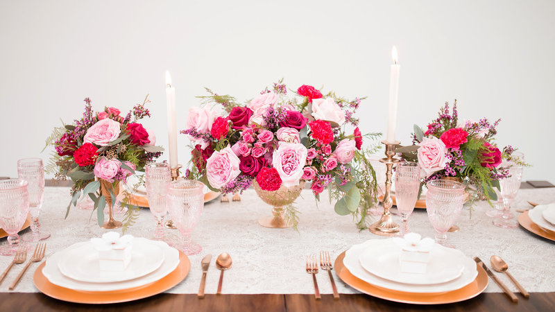 Pink and Fuchsia centerpieces on a textured runner on a wooden table.