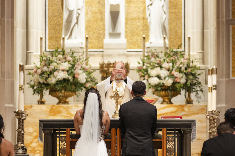 bride and groom standing in front of the priest during a catholic wedding