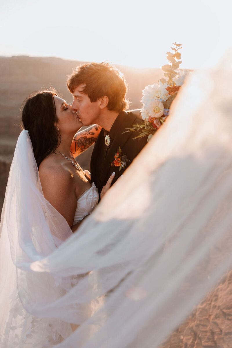 bride and groom kissing in the desdert at sunset with the veil in in the foreground