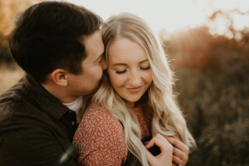 Couple snuggling in golden grass for engagement session