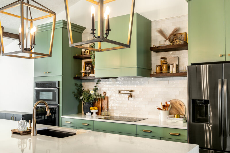  Sage green kitchen with tall oven and refrigerator surround cabinets, custom square range hood with floating shelves. Large custom island with waterfall countertops and counter height bar stools.