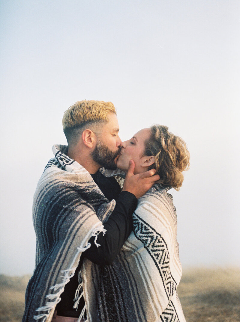 A couple shares a romantic kiss at the beachside in Half Moon Bay, California, captured by Tiffany Longeway Photography.
