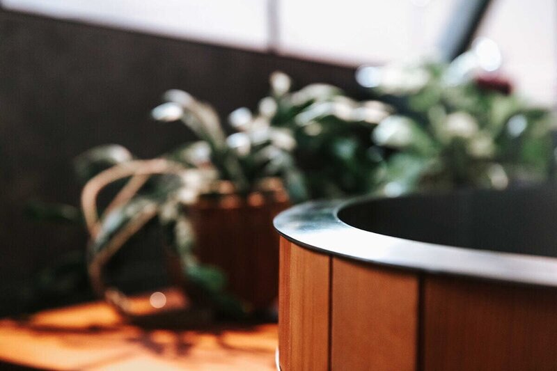The edge of a circular wooden hot tub at a gym with beautiful plants in the background.