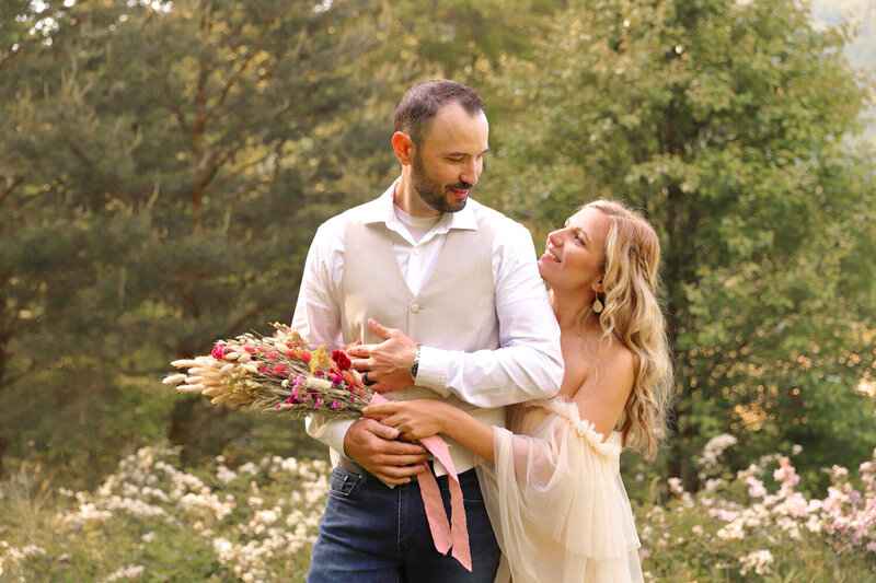 Man looking lovingly at his wife  with her arms around him and holding spring flowers