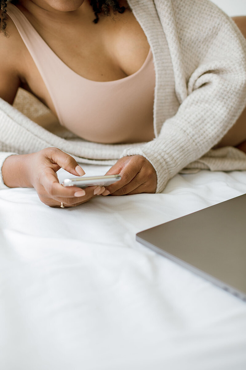 an image of a black woman on her phone on a website for therapy and coaching for moms of color