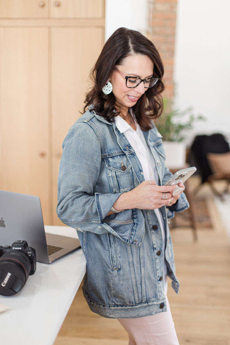 Woman standing next to desk typing on her phone