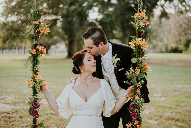 Groom kisses bride's forehead on floral wedding swing at Casa Lantana Brandon FL