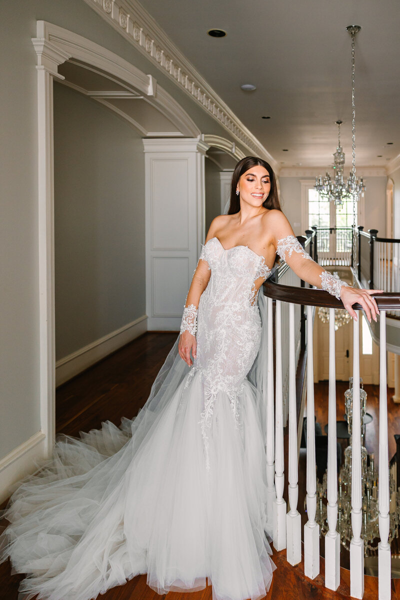Portrait of a bride in an elegant lace dress leaning against a stair railing