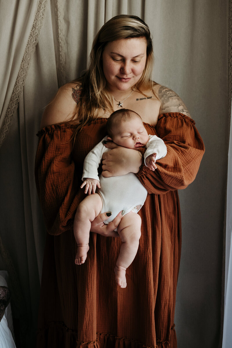 Mom wearing orange boho dress while holding her 3 month old newborn baby boy in dark and moody lifestyle studio in Annapolis Maryland.