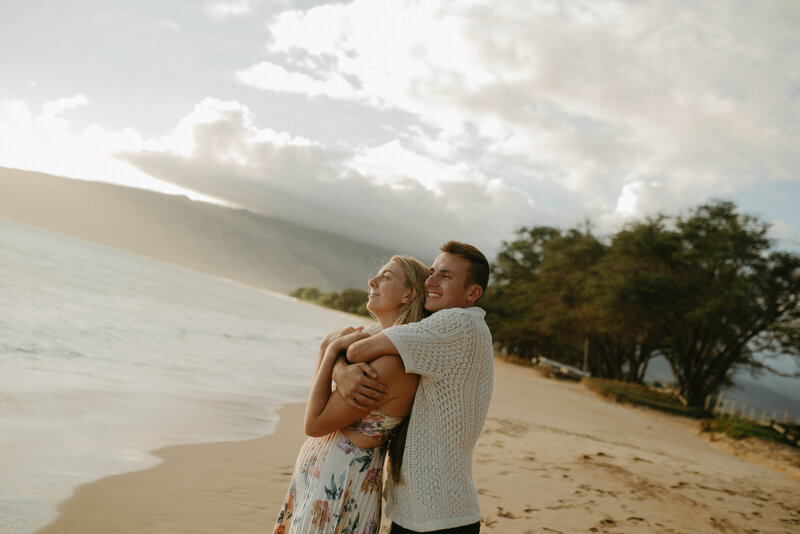 Couple snuggling on a Maui Hawai'i beach, enjoying the ocean views and a romantic moment by the sea.