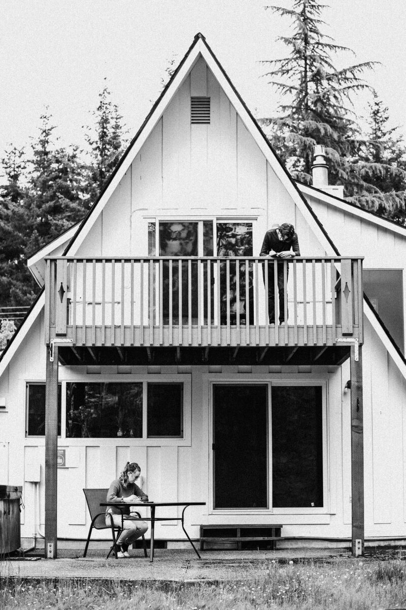 in black and white, a couple writes their vows seated outside of their a-frame cabin during their Olymmpic National Park Elopement.