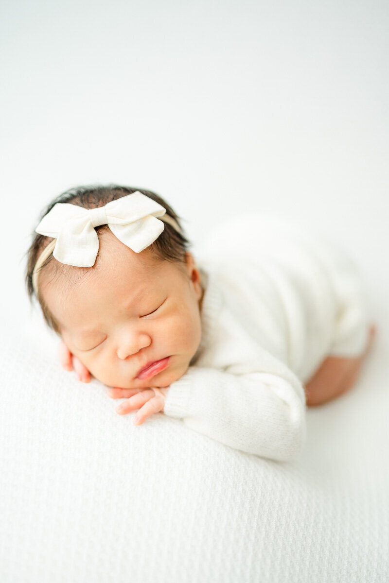 a sleeping newborn girl lays on a white sheet while captured by a newborn photographer in Austin, TX.
