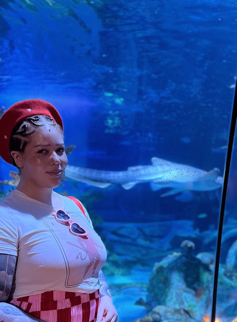 Corie,a private nail tech in South Mountain, AZ, standing in front of a large shark aquarium