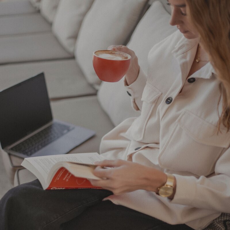 Kylah Jasmine the lead copywriter of The Copy Tribe drinking coffee, reading a book and smiling.