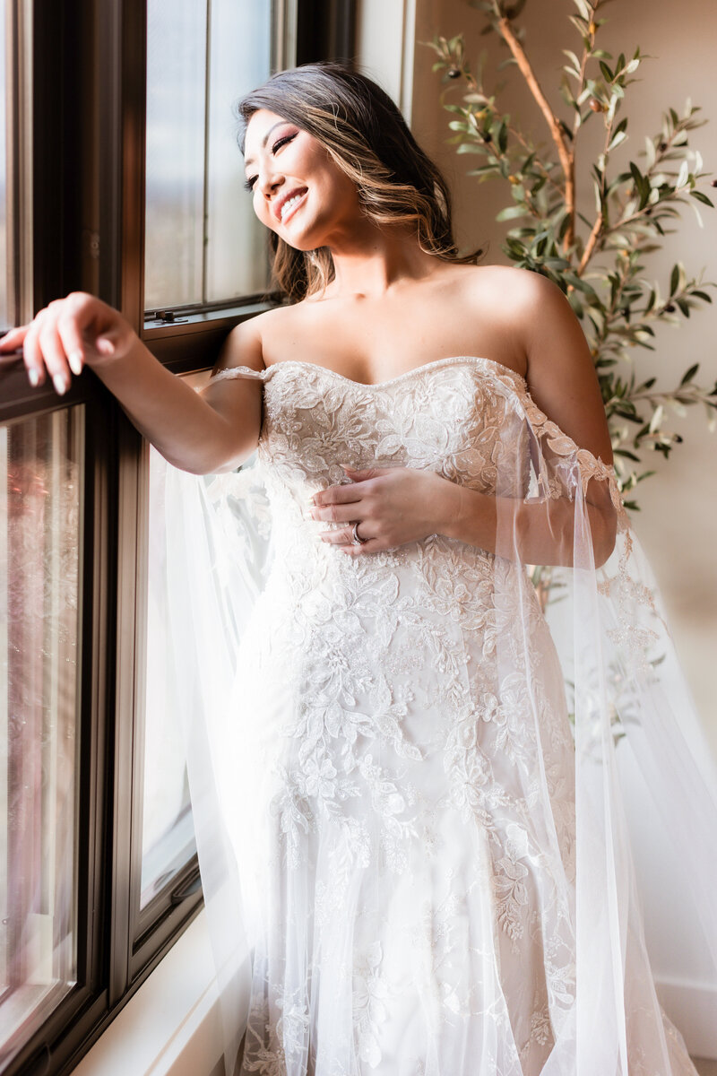 A bride stands ready in front of a window, enjoying that natural light.
