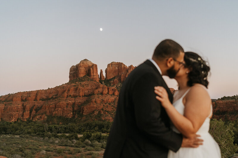 A newlywed couple kissing in front of red rocks 