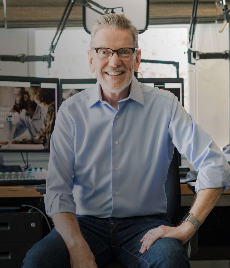 Michael Hyatt sitting in his home studio at a desk with dual monitors, key lights, and a microphone arm in behind him.