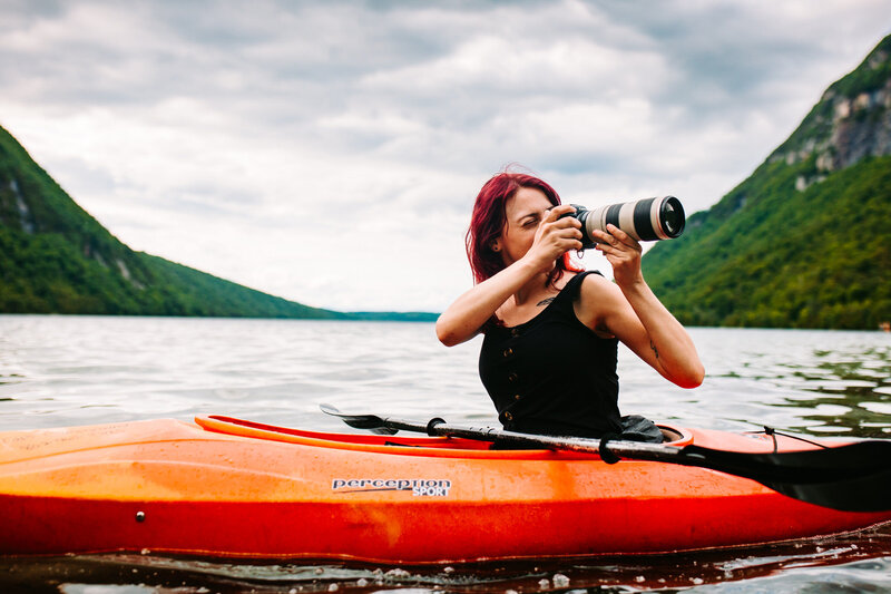 A connecticut wedding photographer on a red kayak in a lake holding a camera