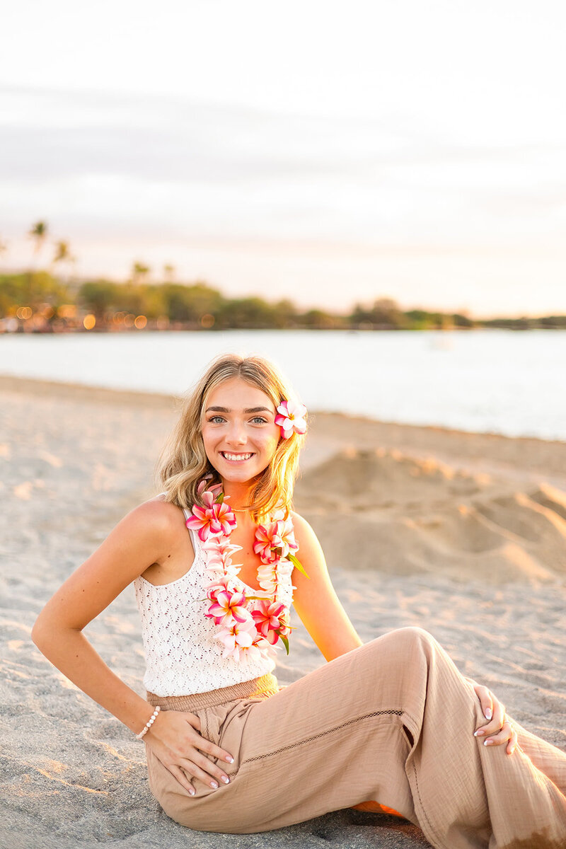high school senior girl sitting posing on the sand at sunset with colorful and warm sunset colors