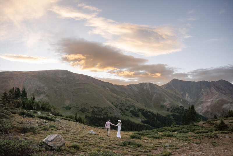 a bride and groom walking during sunrise on a mountain in colorado