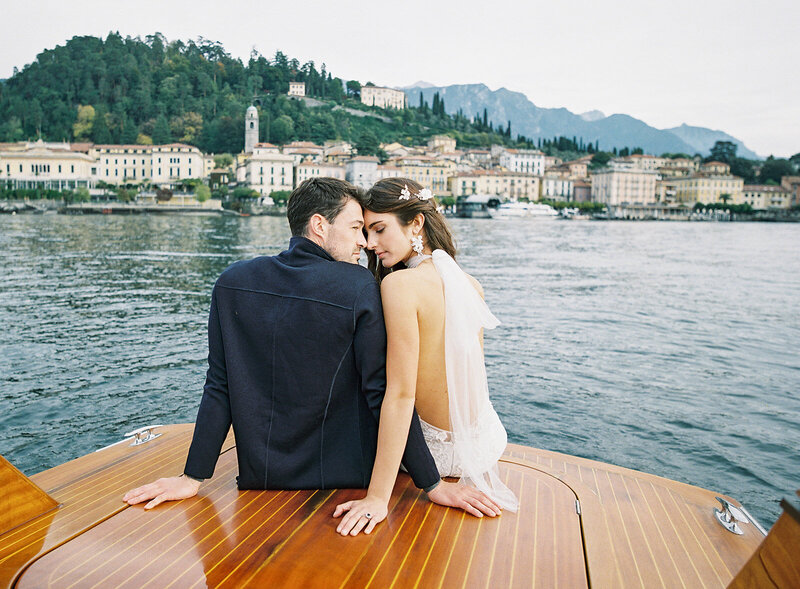 Bride and groom in couple's session on a wooden boat on Lake Como with Bellagio on the background photographed by Italy Wedding photographer