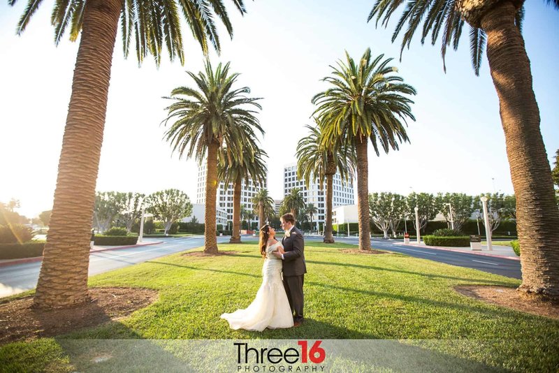 Bride and Groom hold each other under the palm trees in front of the Hotel Irvine wedding venue