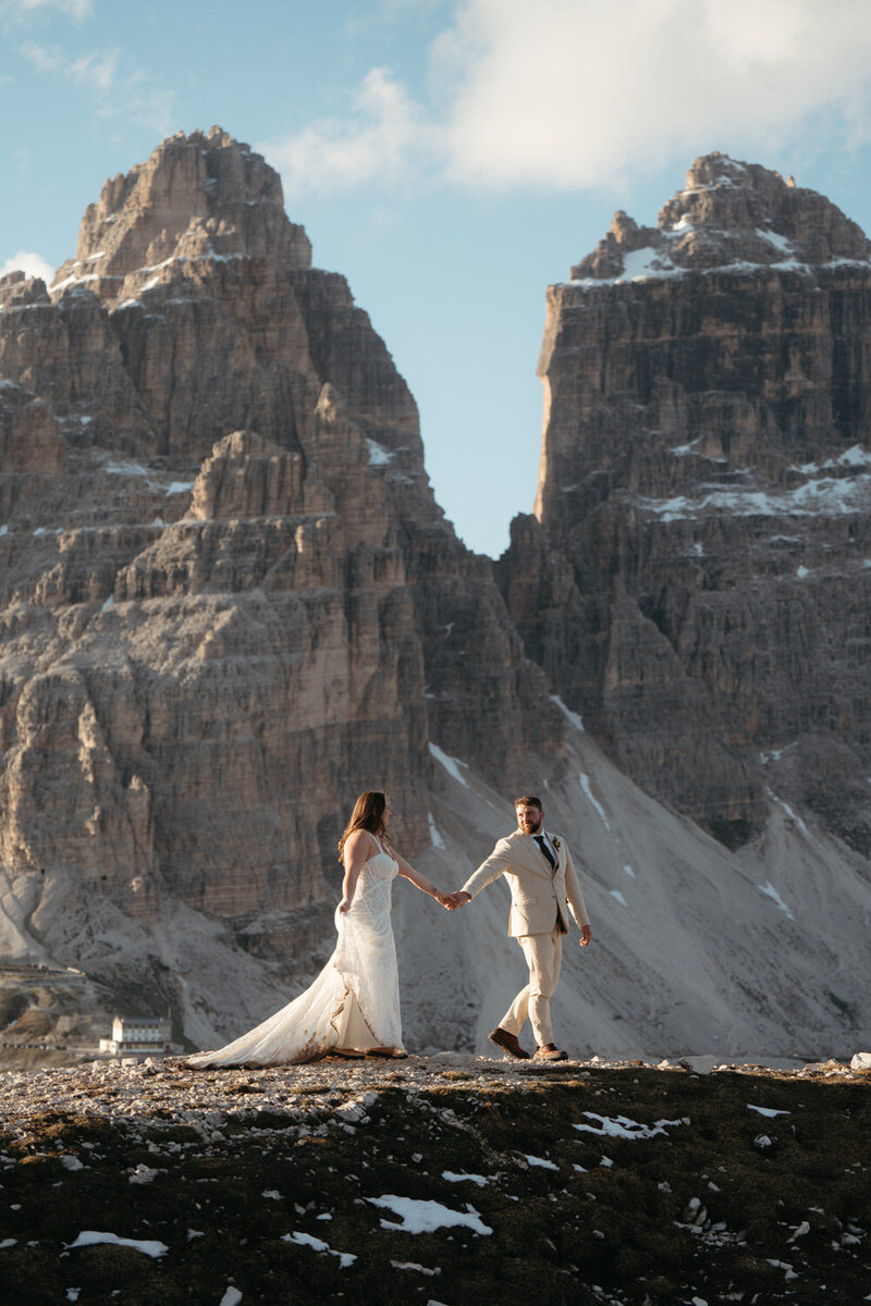 Dolomites Elopement | Groom leads bride by the hand along a mountain ridge with Tre Cime in the background