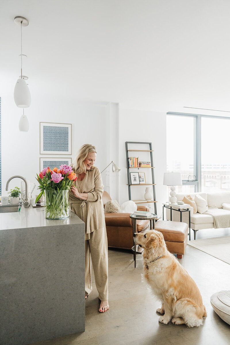 woman arranges flowers in kitchen with golden retriever