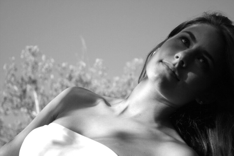 A black and white close-up of a woman looking at the sky in dappled natural light, an example of Courtney's editorial, lifestyle, and portrait photography