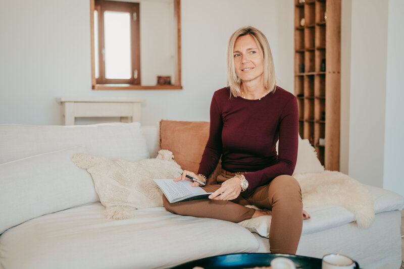 Sylke reflektierend auf dem Sofa mit einem Notizbuch in den Händen