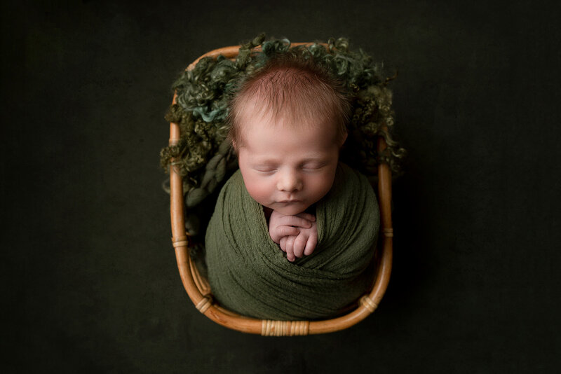 Newborn baby boy in basket with green backdrop