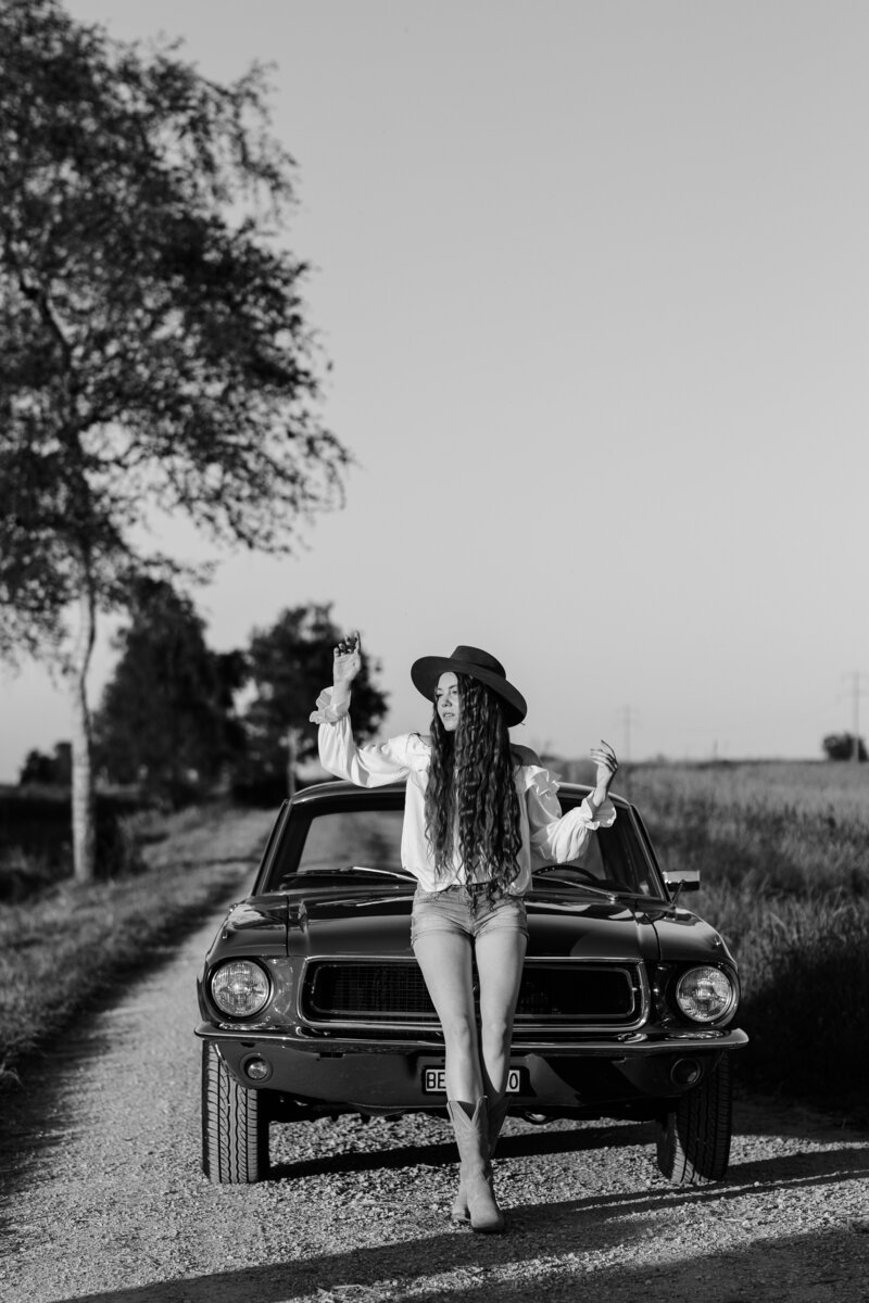 Schwarz-weiss Foto eines weiblichen Models im Western Look vor einem 1968 Ford Mustang