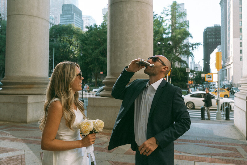 groom taking a shot from a flask outside of city hall after eloping bride and groom after NYLP elopement outside shot by Elsie Goodman Photography | NYC Elopement Packages