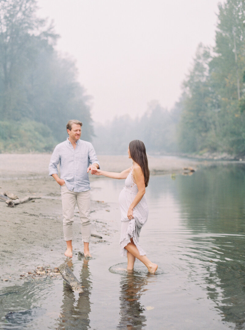 Couple holds hands during maternity photos on film on the river in North Bend, WA on a foggy day. 