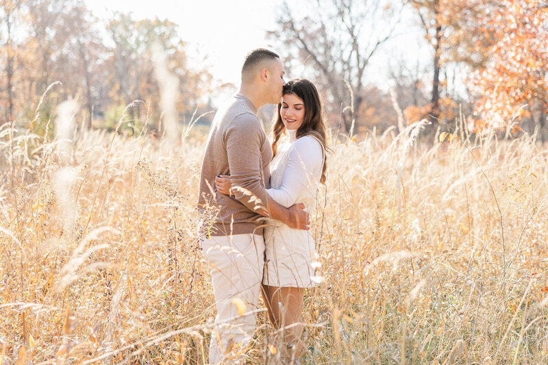 A couple embraces while standing in a field with tall grass