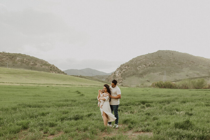 Family photoshoot in nature: mom holding the child, while the husband stands behind her, embracing both