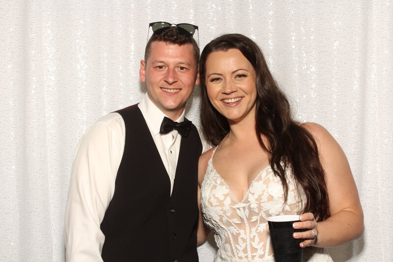 bride and groom standing in front of wedding photo booth backdrop