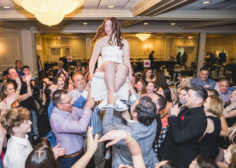 Girl on chair being carried in the air at a Bat Mitzvah party