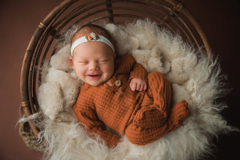 newborn baby girl in fall color sleeping but smiling