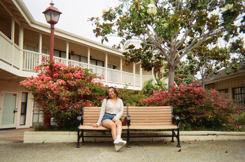 Virtual Assistant Vanessa sitting at a bench in Northen California with trees and buildings.