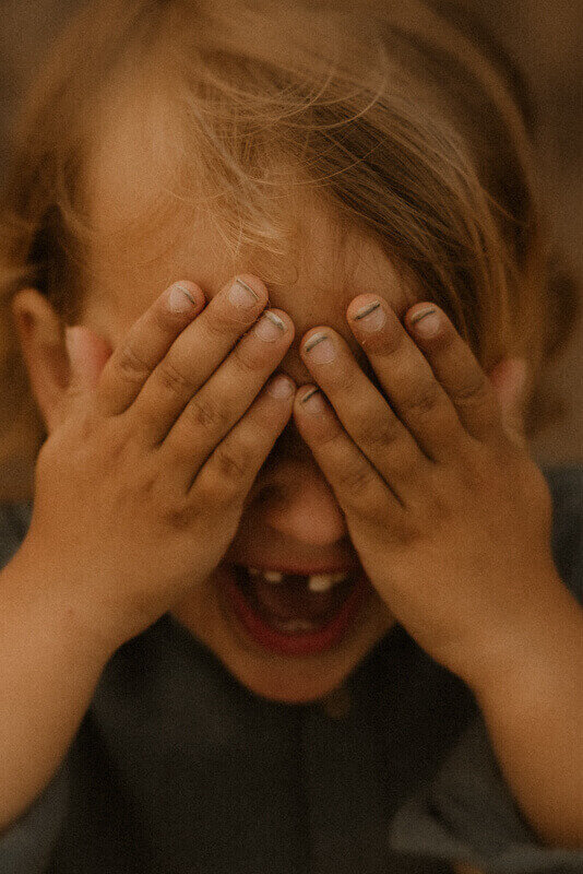 un petit garcon se cache les yeux pour ne pas etre vu par la photographe