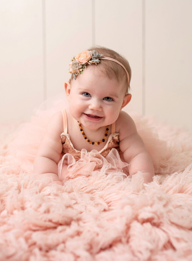 Six month old girl smiles at her baby photo session