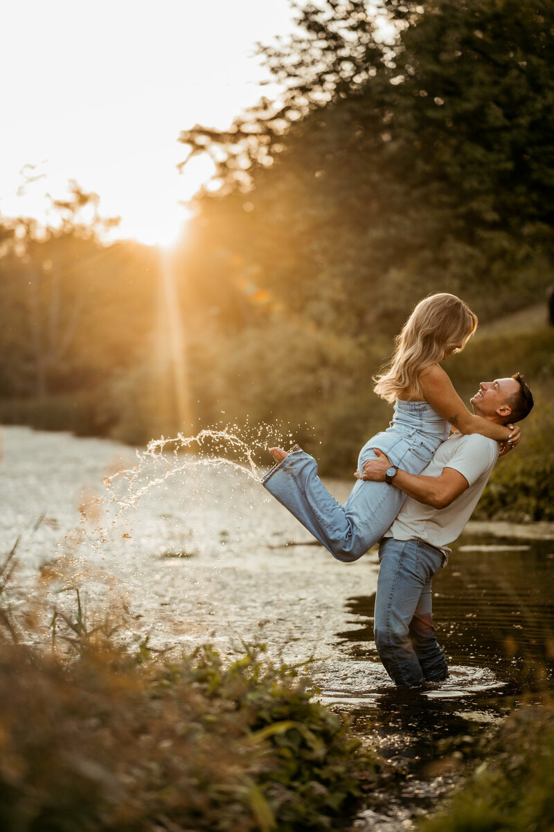 A man squeezing and lifting his new fiance in the air while standing in a river. 