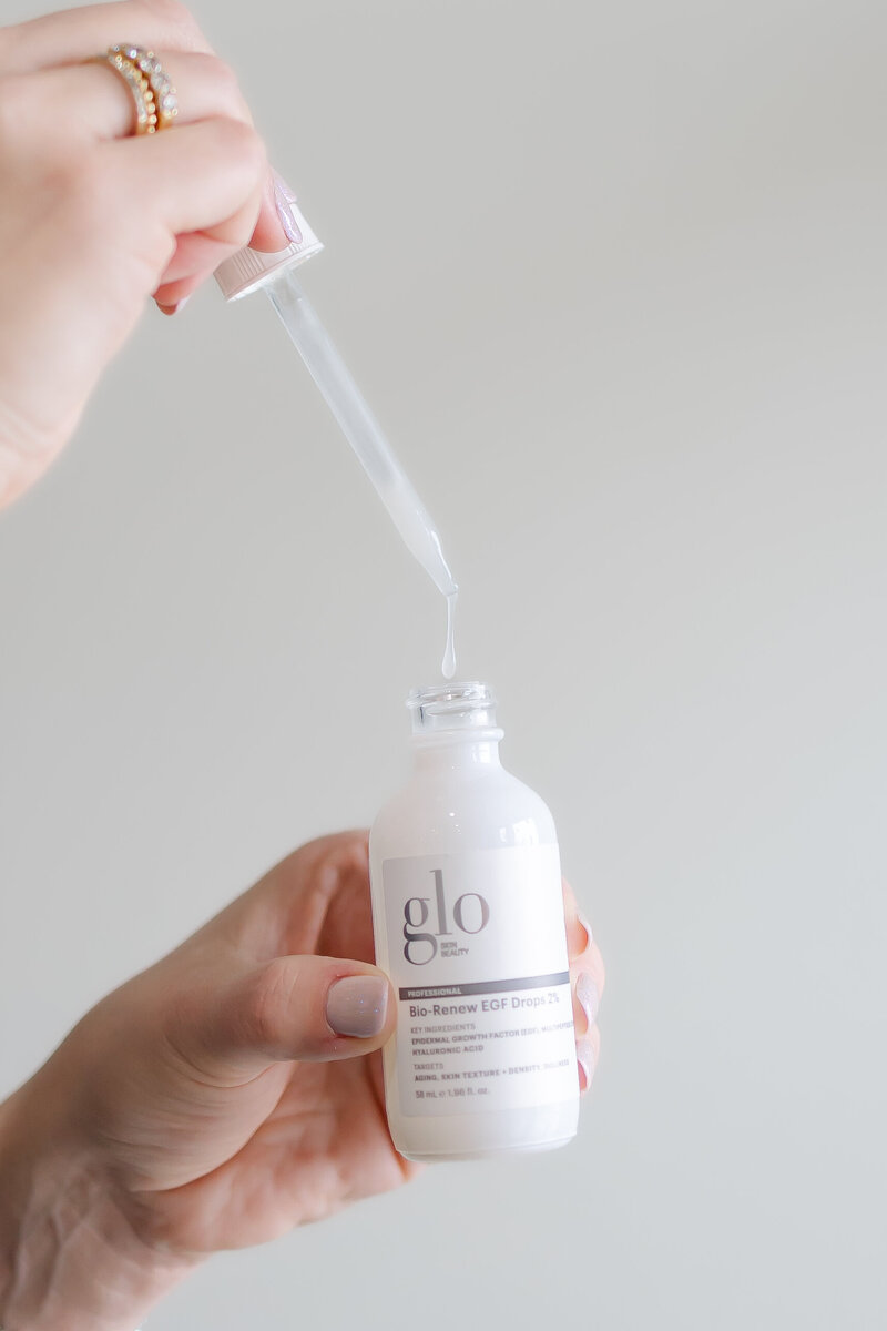 a skincare bottle dropper is pulled out of the bottle and squeezing liquid back into the bottle against a white backdrop