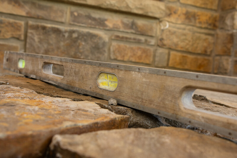 Close-up of a level tool resting on natural stone during patio installation, highlighting craftsmanship and precision by Better Lawns and Gardens in Little Rock, Arkansas.
