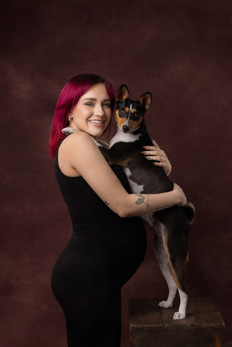 Pregnant woman with bright pink hair holding her Basenji dog during a fine art studio maternity session in Las Vegas by Angela Wolf Photography